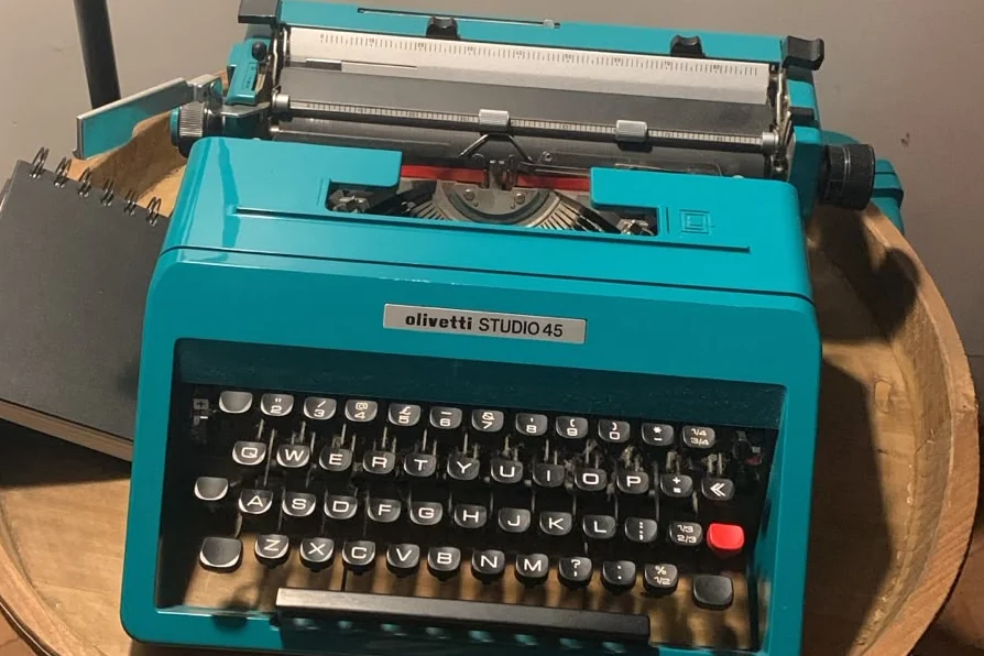 A turquoise Olivetti typewriter on a round wooden table
