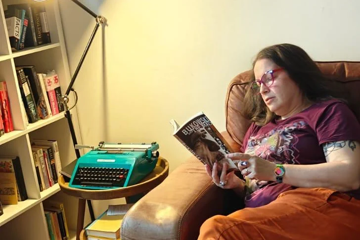 Someone reading in an armchair at the studio, beside a typewriter and the bookshelves
